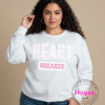 Woman wearing a white sweatshirt with 'HEART BREAKER' text, standing against a beige background.