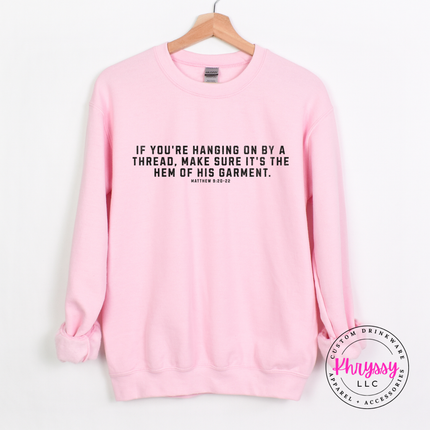 Light Pink crewneck sweatshirt on a hanger with black hem of His garment verse