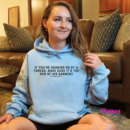 Folded Light Blue hoodie with the hanging on by a thread verse in black