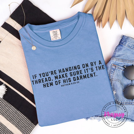 Folded Blue Jean tee printed with the hanging on by a thread verse in black