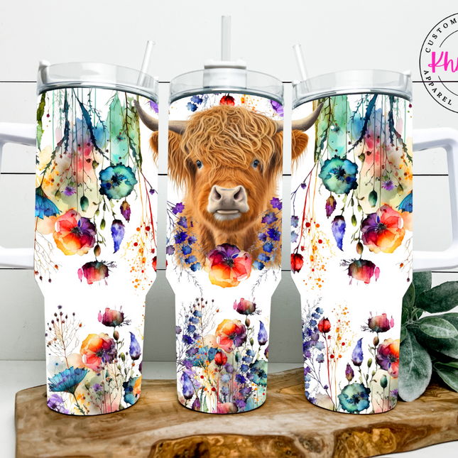 A 40oz stainless steel tumbler with a double-wall vacuum insulation feature. The tumbler is adorned with a colorful sublimation print of a Highland cow amidst wildflowers.