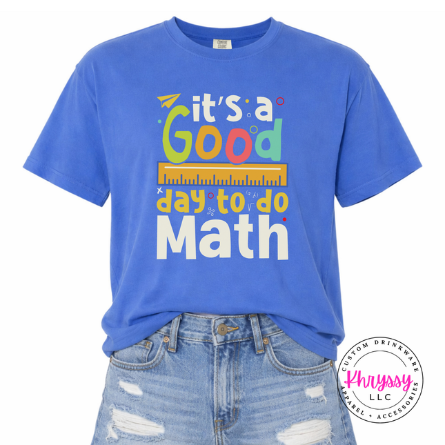 Mystic Blue Comfort Colors tee showing bright multicolor math teacher statement with ruler and colorful letter detail.