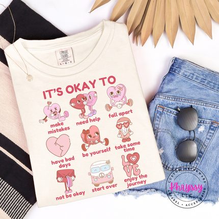 Ivory t-shirt with motivational graphics and text, placed on a white surface with denim jeans and sunglasses.