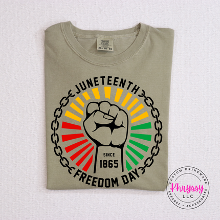 Khaki garment-dyed tee showing a black raised-fist Pan-African Juneteenth graphic.