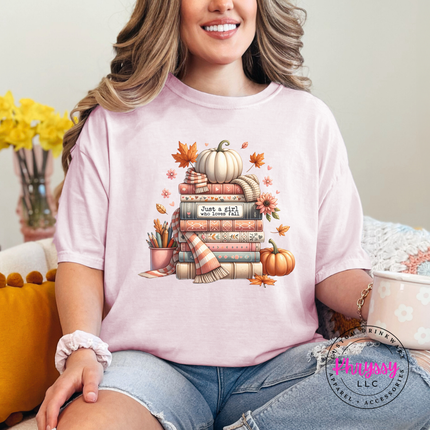 Woman wearing a Blossom tee with a cozy book stack and white pumpkin.