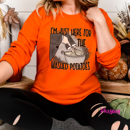 Woman wearing an orange crewneck sweatshirt with a mashed potatoes design.