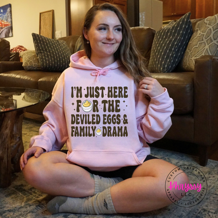 Woman wearing a light pink heavyweight hoodie with a deviled eggs family drama graphic.