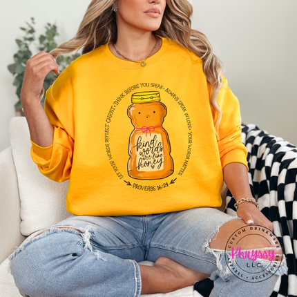 Woman wearing a gold sweatshirt with a honey jar graphic and text, sitting on a couch.