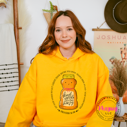Woman wearing a yellow hoodie with a bear and text design, standing in a home decor setting.