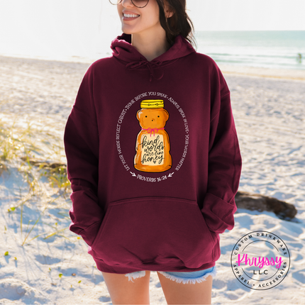 Person wearing a maroon hoodie with a honey bear graphic on a sandy beach.