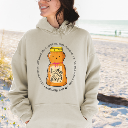 Person wearing a beige hoodie with a honey jar graphic and text on a beach.