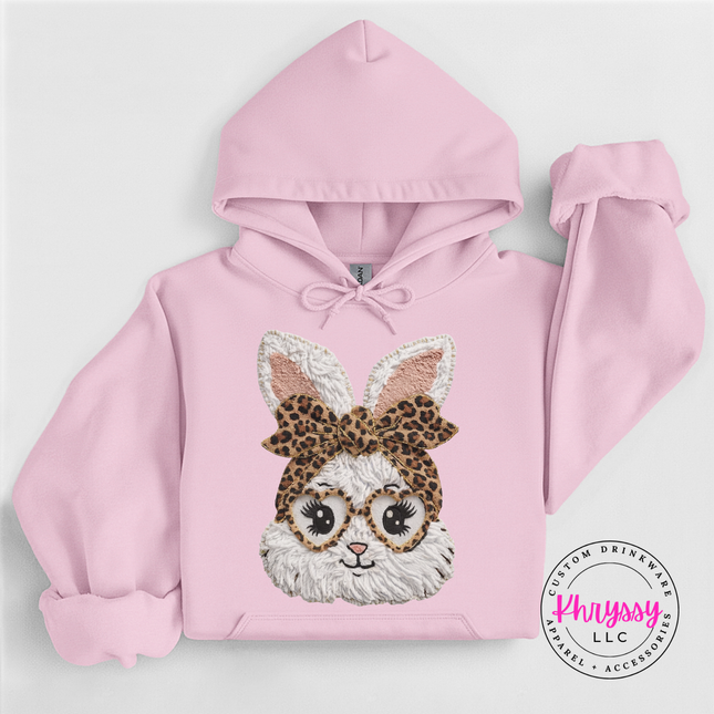 Pink hoodie with a bunny design wearing glasses and a leopard print headband on a light gray background.