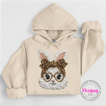 Sand hoodie with a bunny face design wearing glasses and a leopard print bow, on a light gray background.