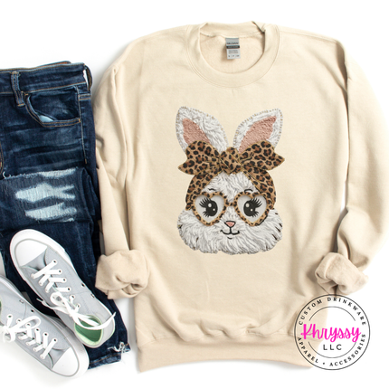 Sand sweatshirt with a rabbit design wearing glasses and a leopard print headband, paired with jeans and sneakers.