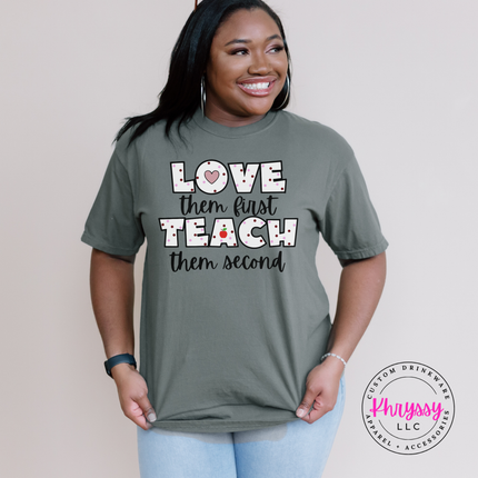 Bold love them first teach them second educator statement on Sage Comfort Colors tee with playful apple graphic