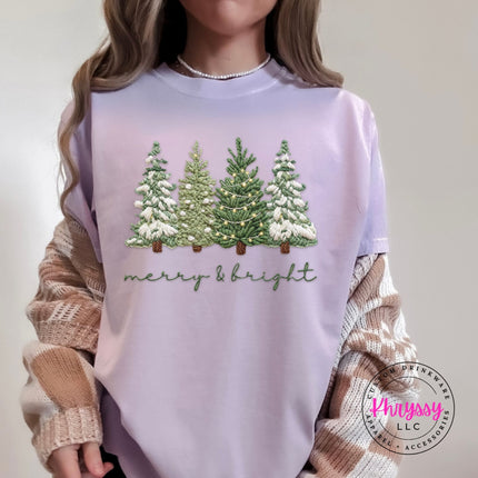 Orchid Comfort Colors tee showing four snowy evergreen trees above soft script lettering.