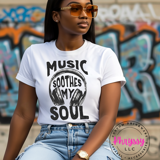 Woman wearing a white t-shirt with 'Music Soothes My Soul' design in front of graffiti.