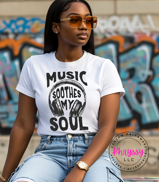 Woman wearing a white t-shirt with 'Music Soothes My Soul' design in front of graffiti.