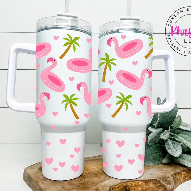 white tumbler with pink flamingo float graphics, palm trees, and hearts- includes handle, lid, and straw.
