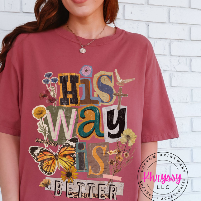 Person wearing a maroon t-shirt with decorative text and graphics against a white brick wall.