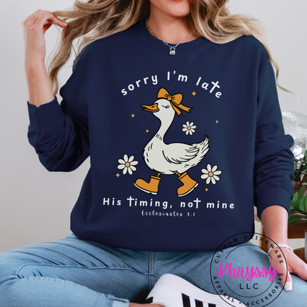 Person wearing a navy blue sweatshirt with a duck graphic and text, sitting on a chair.