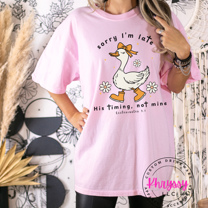 Person wearing a pink t-shirt with a graphic and text, standing against a decorative background.