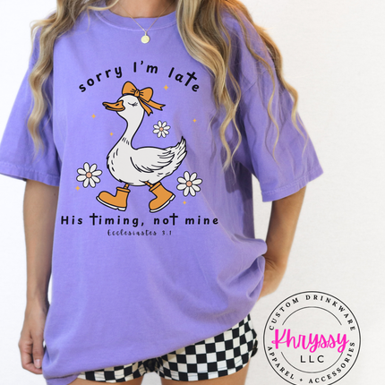 Person wearing a purple t-shirt with a graphic of a duck and text, standing against a white background.