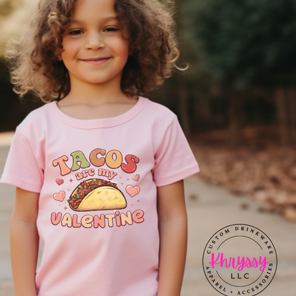 Child wearing a pink t-shirt with a taco design and text, standing outdoors.
