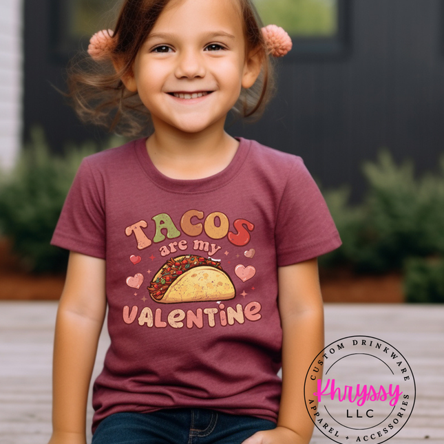 Child wearing a shirt with 'Tacos are my Valentine' text, sitting outdoors.
