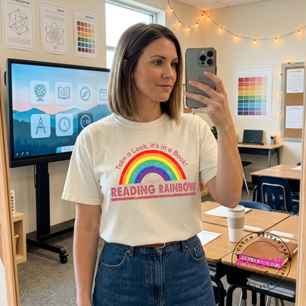Teacher in an ivory tee with a retro Reading Rainbow book design.