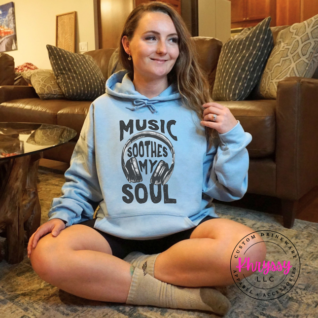 Person wearing a hoodie with 'Music Soothes My Soul' text sitting on a couch.