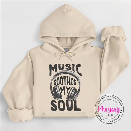Beige hoodie with 'Music Soothes My Soul' text and headphones graphic on a light gray background, featuring the brand 'Khryssy LLC'.