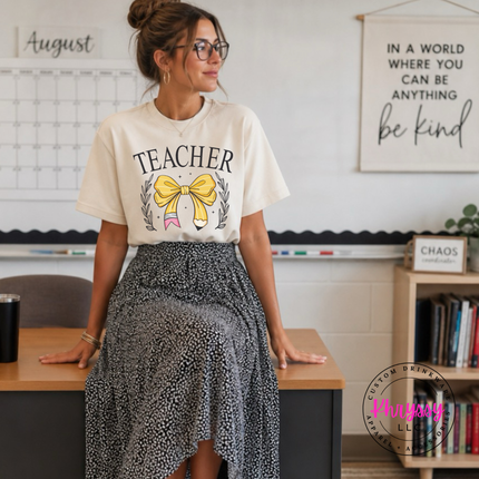 Elegant teacher graphic with gold bow shown on an Ivory colored tee.