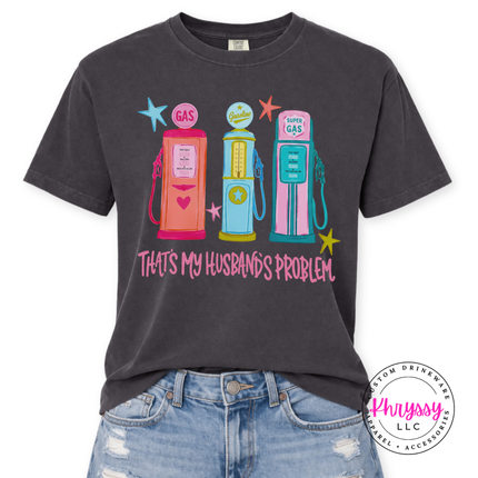 Black t-shirt with colorful gas pump graphic and text 'That's my husband's problem' on a white background.