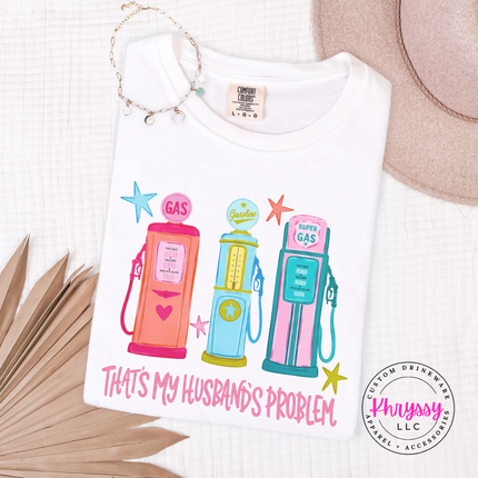 White t-shirt with colorful gas pump design and text 'That's my husband's problem' on a white background.