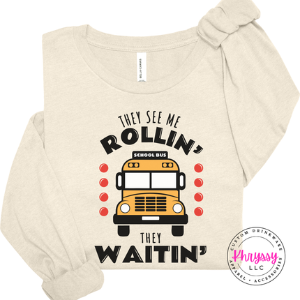 Heather Natural tee styled outdoors, showing the They See Me Rollin quote.