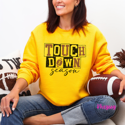 Woman wearing an gold crewneck sweatshirt with a touchdown season design.