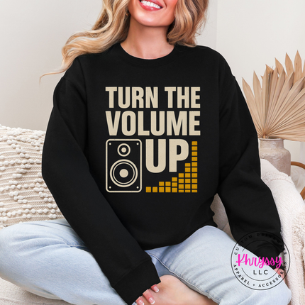 Person wearing a black sweatshirt with 'Turn the Volume Up' text and graphic, sitting on a couch.