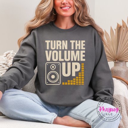 Person wearing a gray sweatshirt with 'Turn the Volume Up' text and graphic, sitting on a couch.