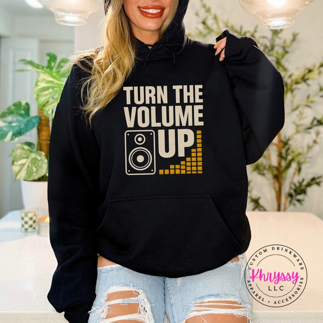 Person wearing a black hoodie with 'Turn the Volume Up' text and graphic, standing indoors.