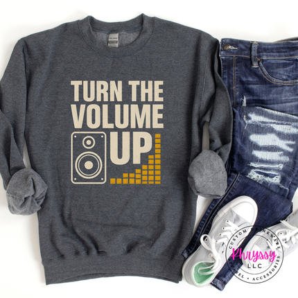 Gray sweatshirt with 'Turn the Volume Up' text and graphic, paired with jeans and sneakers on a white background.