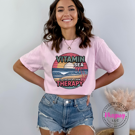 Woman wearing a pink t-shirt with a graphic design and text, standing against a plain background.