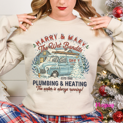 Sand crewneck sweatshirt hanging on a rack, showing a vintage plumbing and heating Christmas graphic.